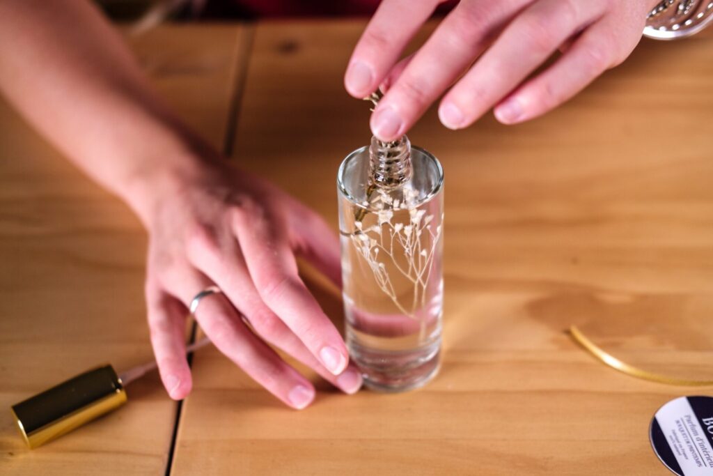 Mains qui glissent des fleurs séchées dans un flacon de parfum d’intérieur, à l’atelier