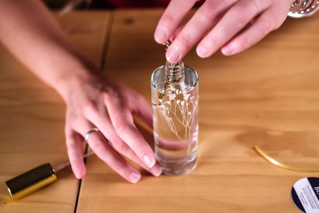 Mains qui glissent des fleurs séchées dans un flacon de parfum d’intérieur, à l’atelier